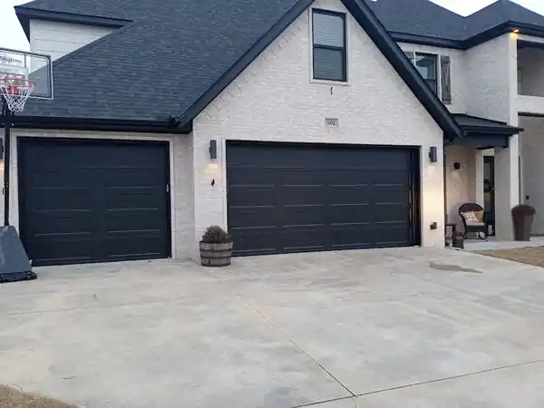A single and a double black garage door on a pale brick house
