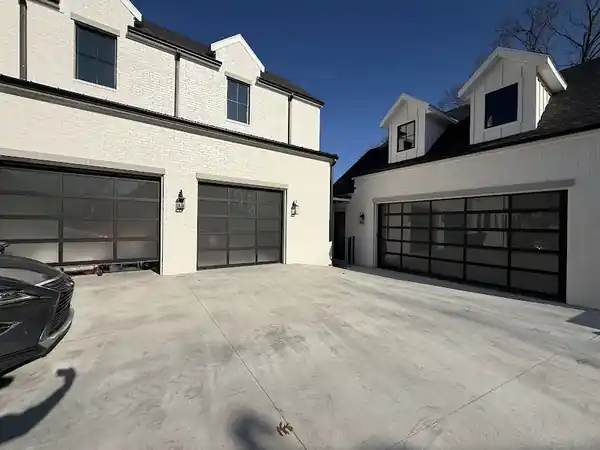 Three full view glass garage doors on a white brick farmhouse, installed by Elite