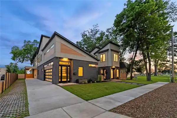 Modern two-house build at dusk with lit full-view garage doors