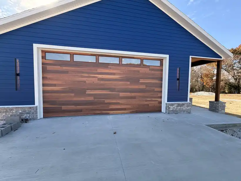 Wood-look plank garage door with a row of glass lites, installed by Elite in deep blue lap siding