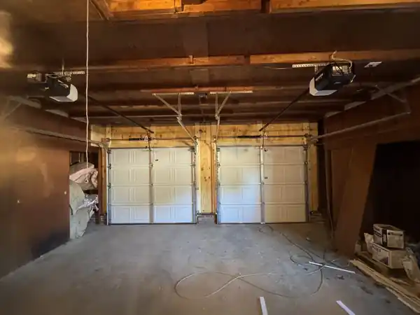 Older wood-framed garage interior with two white doors and two openers