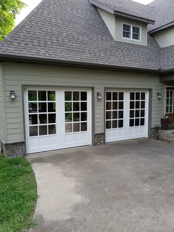 White carriage-style garage doors with colonial glass grids on a sage-green house