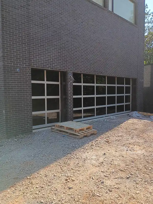 Black-framed full-view glass garage doors, one single and one double, set in dark brick