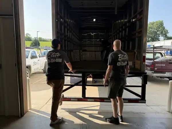 Two Elite technicians loading a flatbed in front of the open bay at the shop