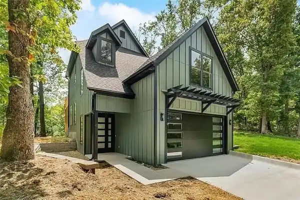 Sage board-and-batten house with a black garage door with a glass stack