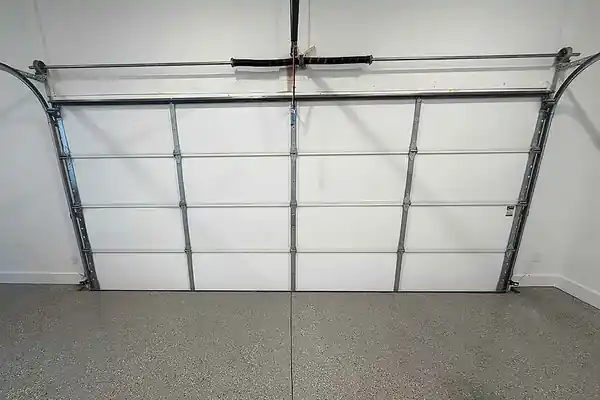 White insulated garage door seen from inside above a flake-epoxy floor