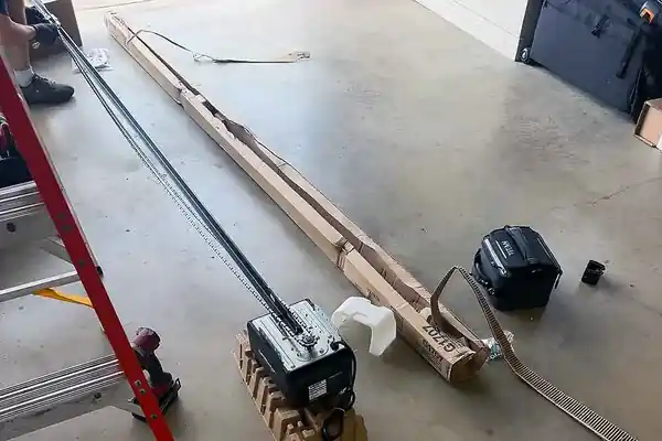 Garage door opener head and rail with a ladder on the floor in the middle of an install
