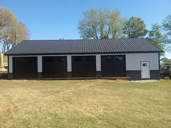 Long white shop building with four black garage doors over a lawn
