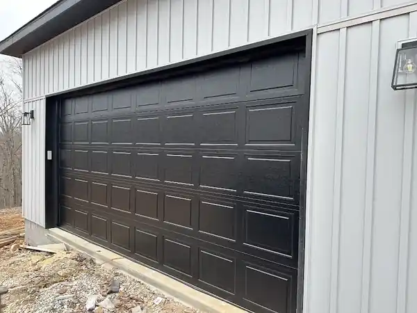 Black raised-panel double garage door on a white board-and-batten building