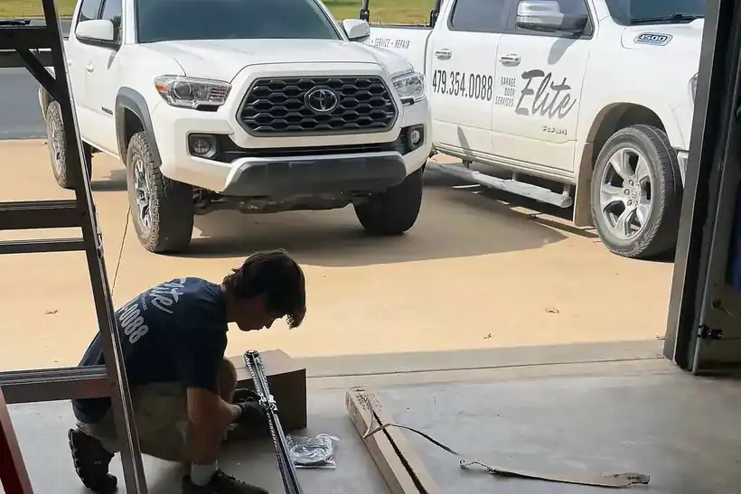 Elite technician assembling a LiftMaster opener rail on a garage floor, company trucks outside