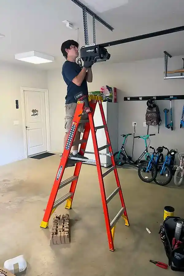 Elite technician on a ladder mounting a LiftMaster opener to a garage ceiling