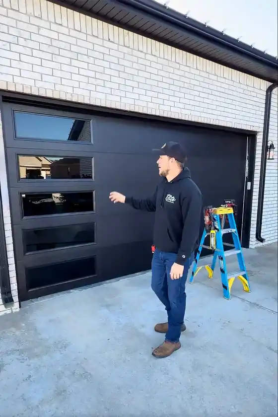 An Elite technician in a company hoodie running a new black full-view garage door after service
