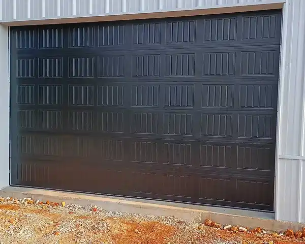 Large black ribbed overhead door in white steel siding